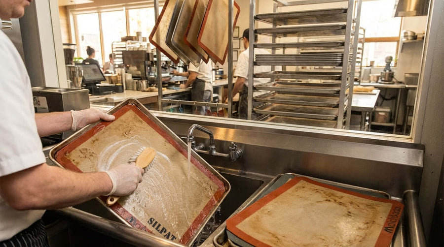 How to Properly Clean and Care for Your Baking Mats to Maximize Lifespan - chef scrubbing silicone baking mats in commercial kitchen sink